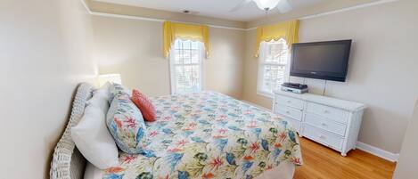 A bedroom with a bed, a TV, a dresser, and a ceiling fan.
