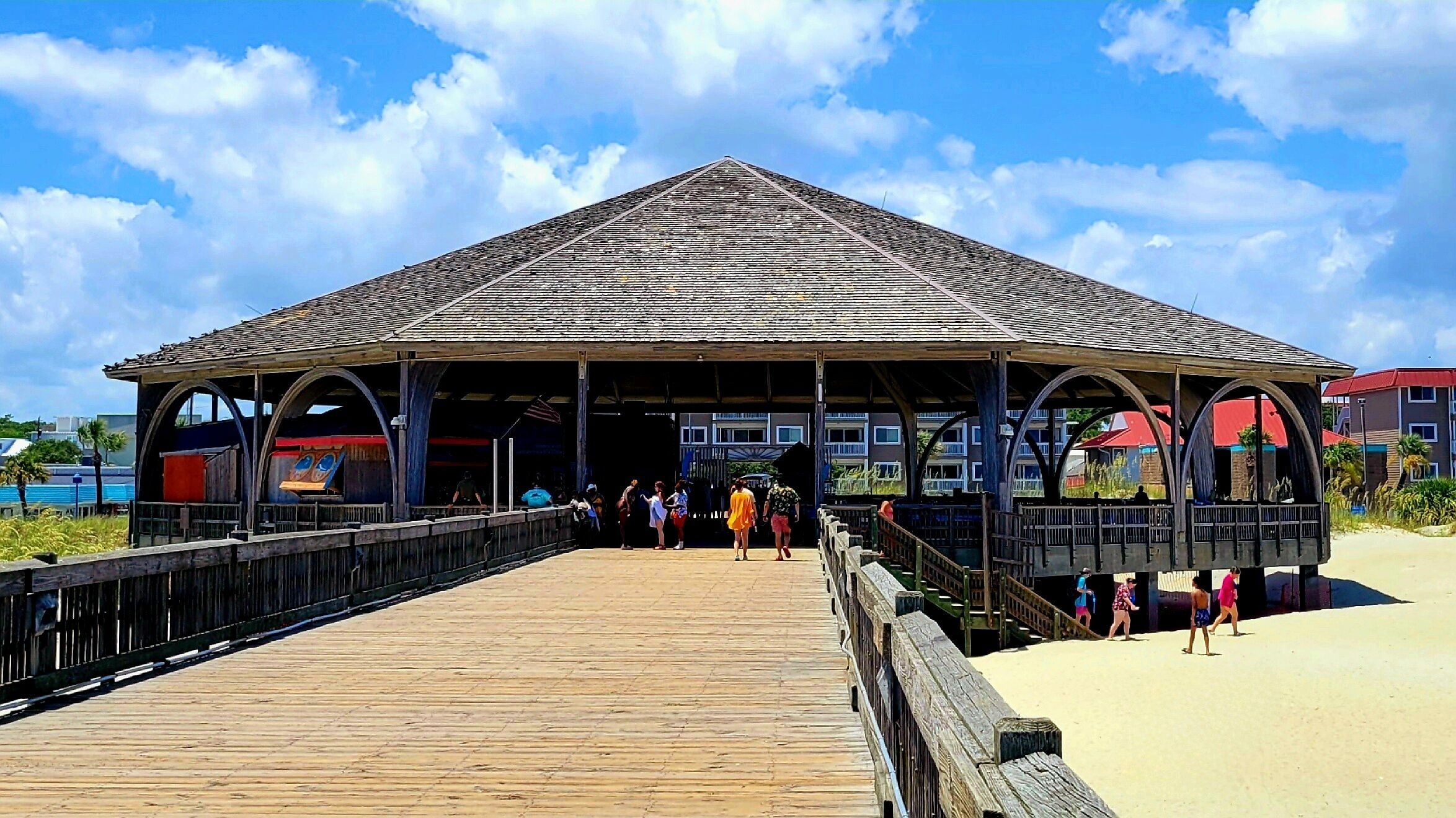 Eine Holzsteg führt zu einem überdachten Pavillon mit geneigtem Dach, mit Blick auf einen Strand.
