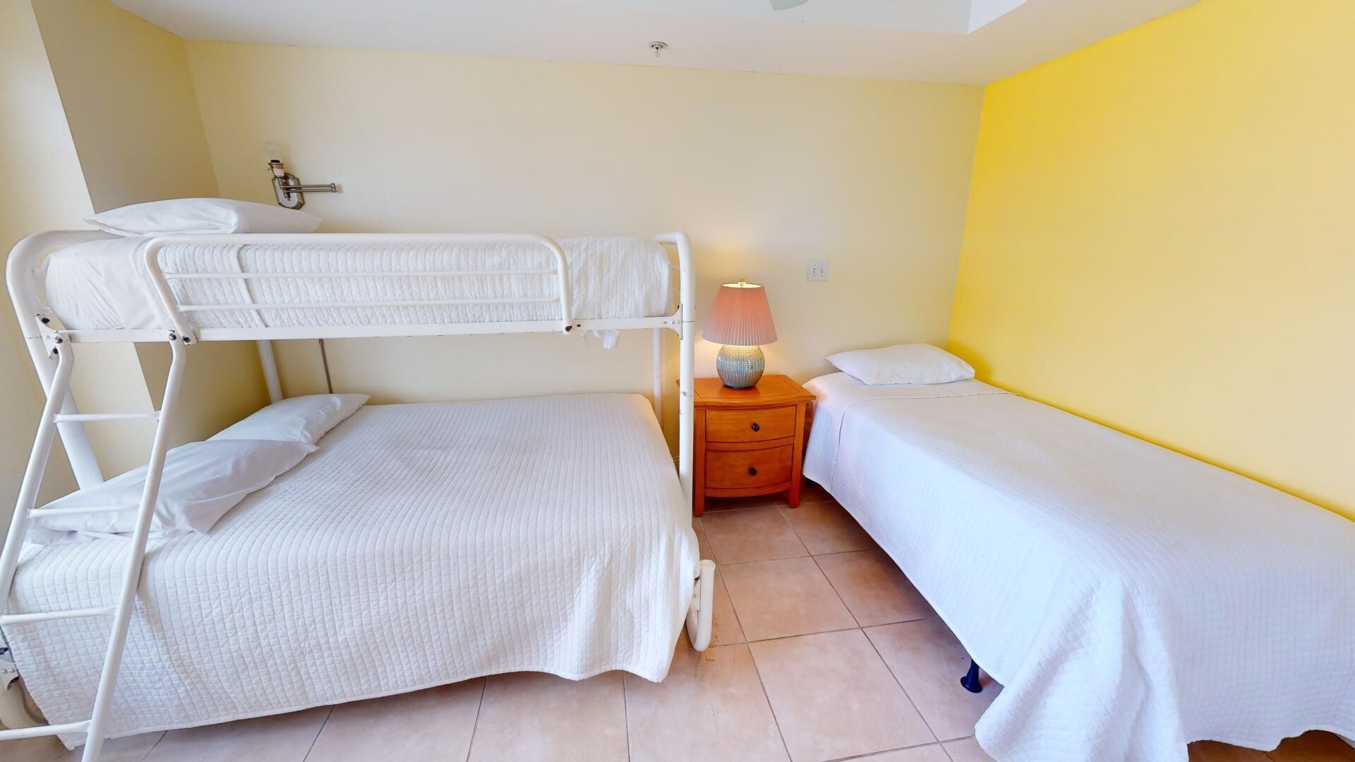A bunk bed room with a single bed and a nightstand with a lamp.