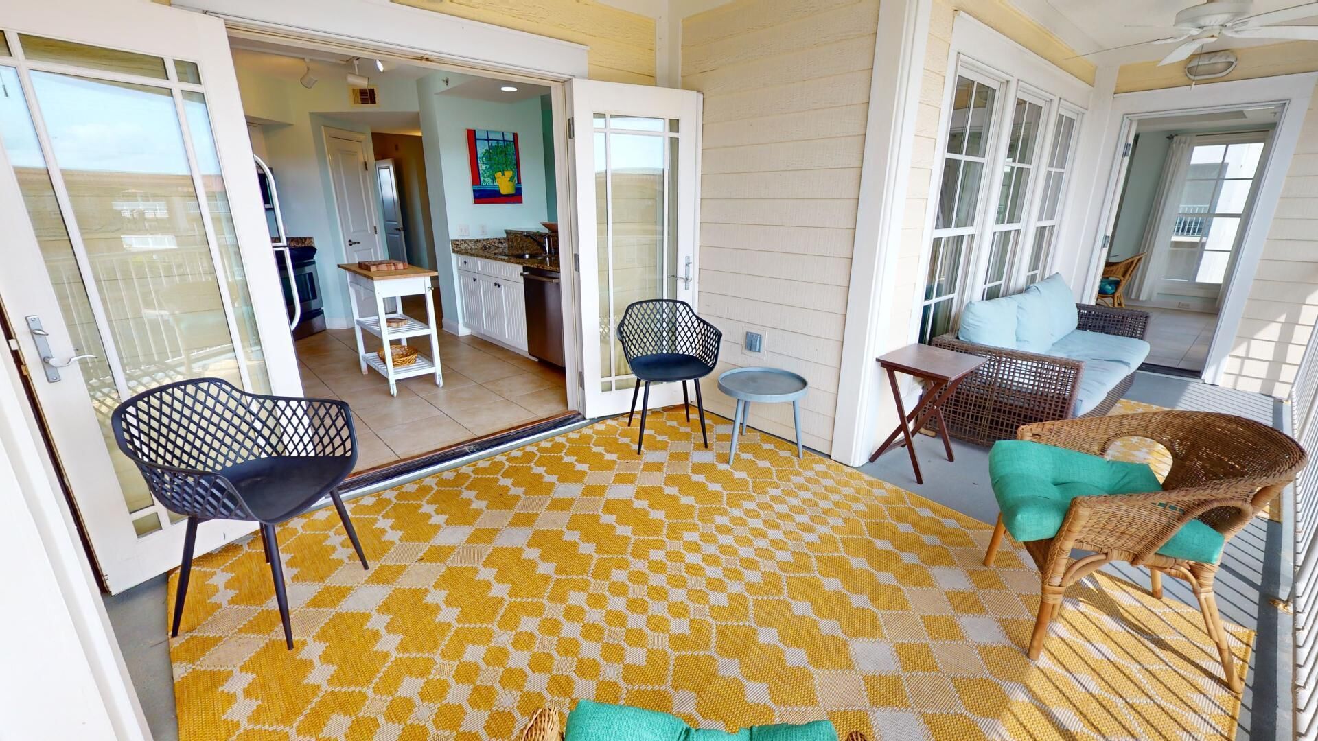 A spacious patio area with a yellow patterned rug, wicker furniture, and a view into the house.