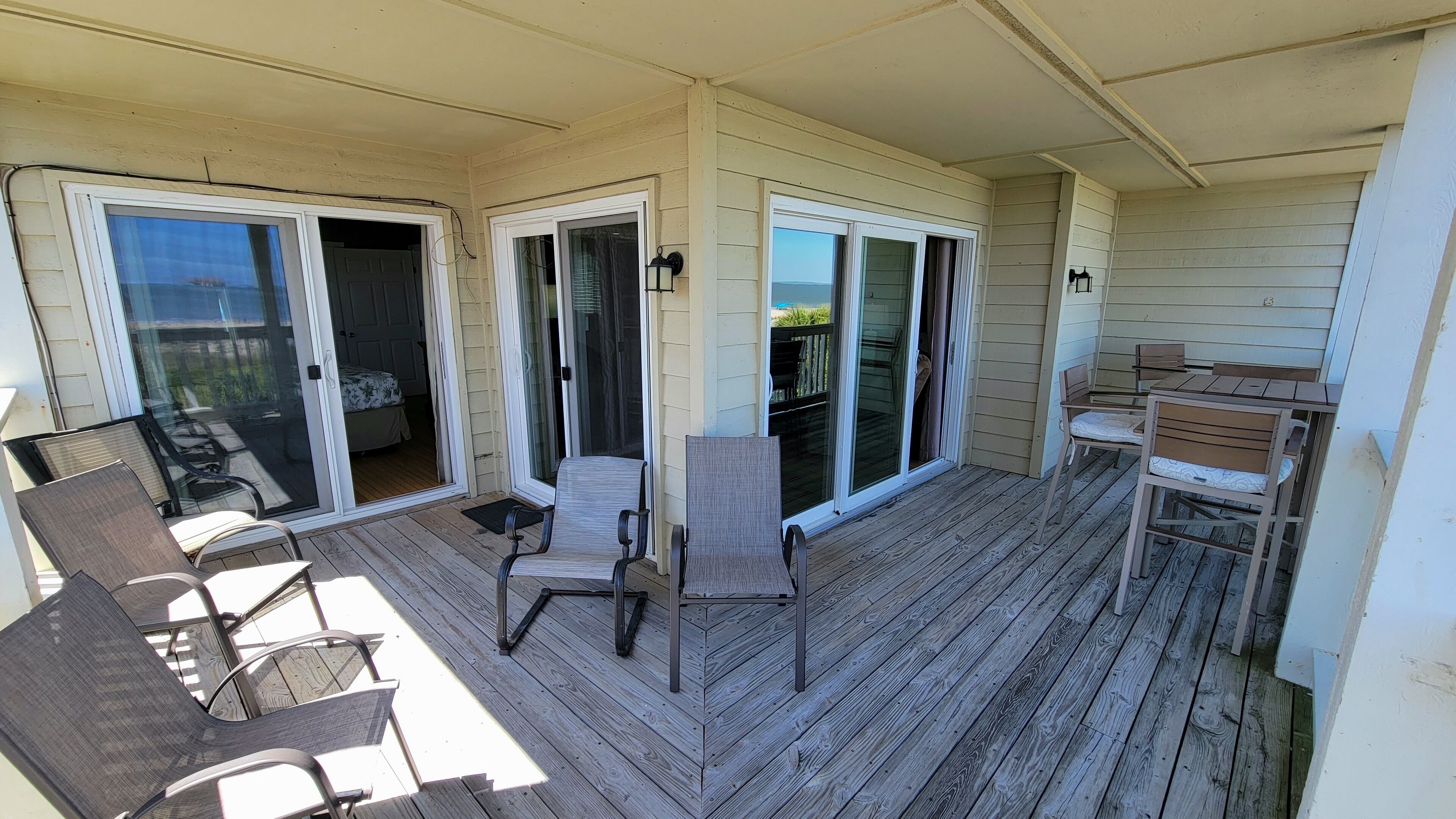 A covered patio with a wooden deck, sliding glass doors leading to a bedroom, and a small table with chairs.
