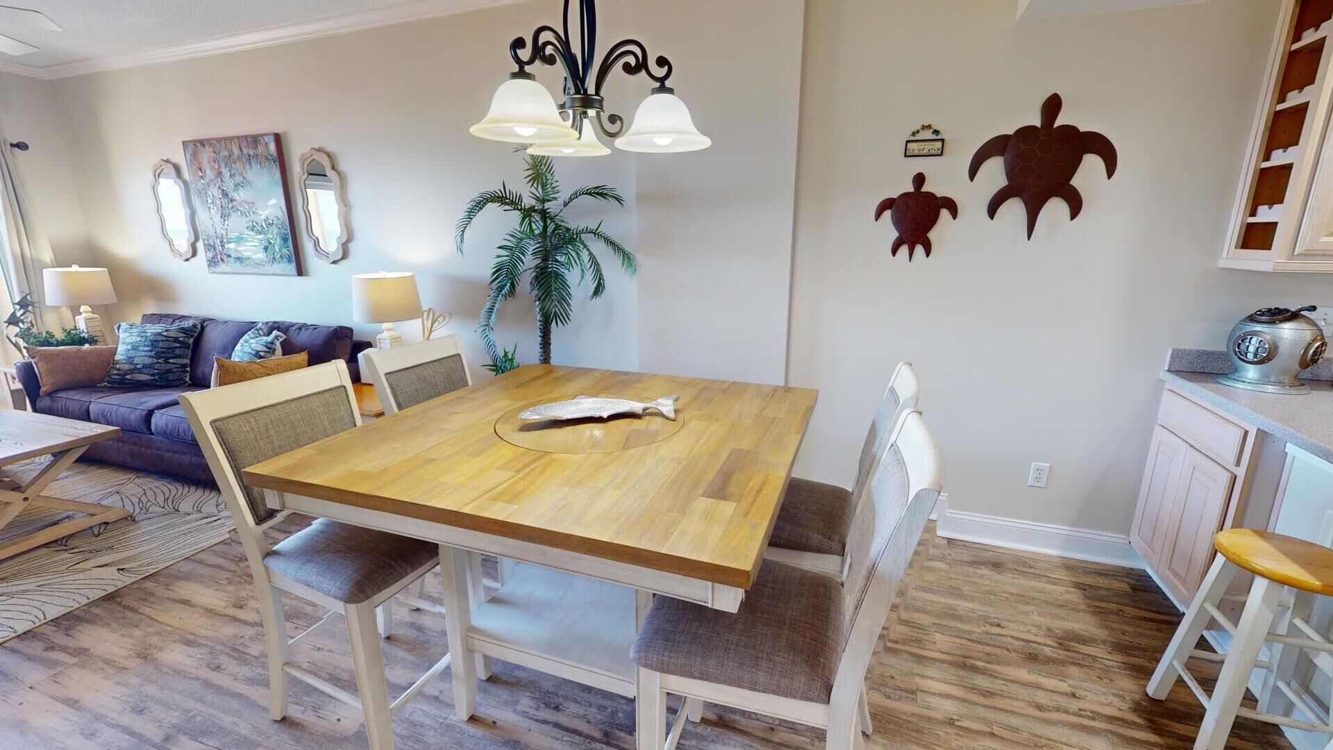 Un comedor con una mesa de madera, sillas blancas, una araña y decoración en la pared.