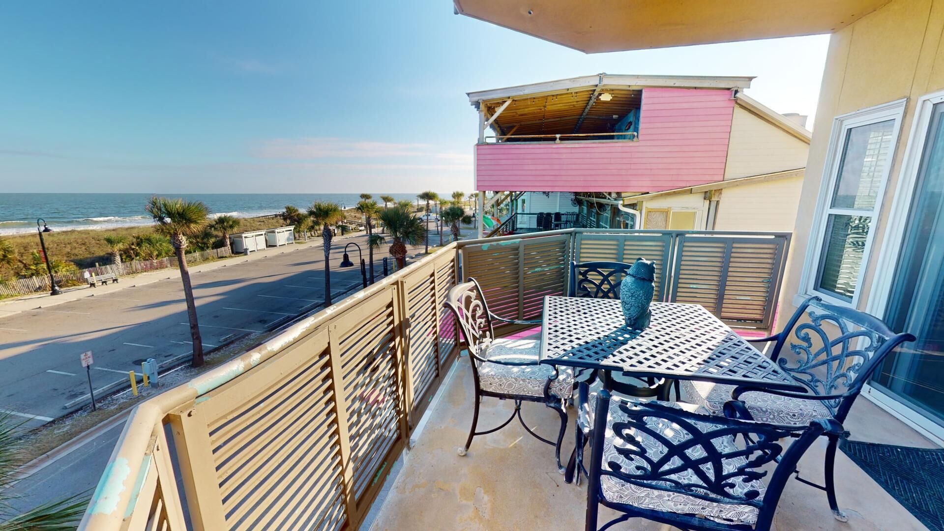 A balcony with a table and chairs overlooking a beach.