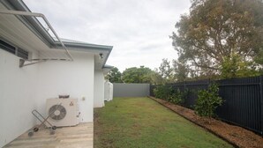 A backyard with a grassy lawn, a black fence, and a white building with a grey roof. - Azure on Bondi Place (Tweed)