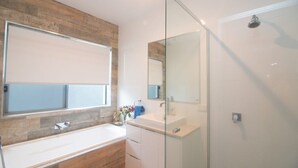 A modern bathroom with a large mirror, a glass shower enclosure, and a wooden accent wall. - Azure on Bondi Place (Tweed)