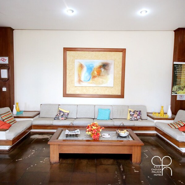 A modern hotel lobby with a large abstract painting, a central coffee table with a floral arrangement, and a seating area with two sofas and multiple cushions.