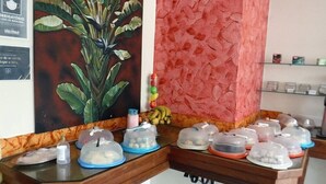 Un mostrador de recepción con una planta grande, una pared texturizada roja y varios recipientes cubiertos con comida.