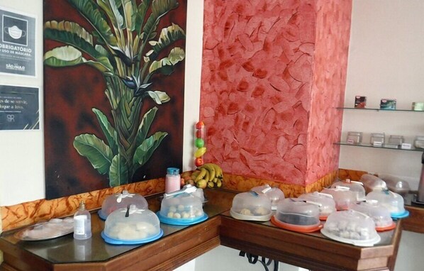 A reception desk with a large plant, a red textured wall, and several covered food containers.