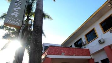 A hotel entrance with a red and white facade, palm trees, and a sign for 'Cazua Palace Hotel'.