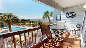Varanda com vista para piscina e oceano, mobiliada com mesa e cadeiras.