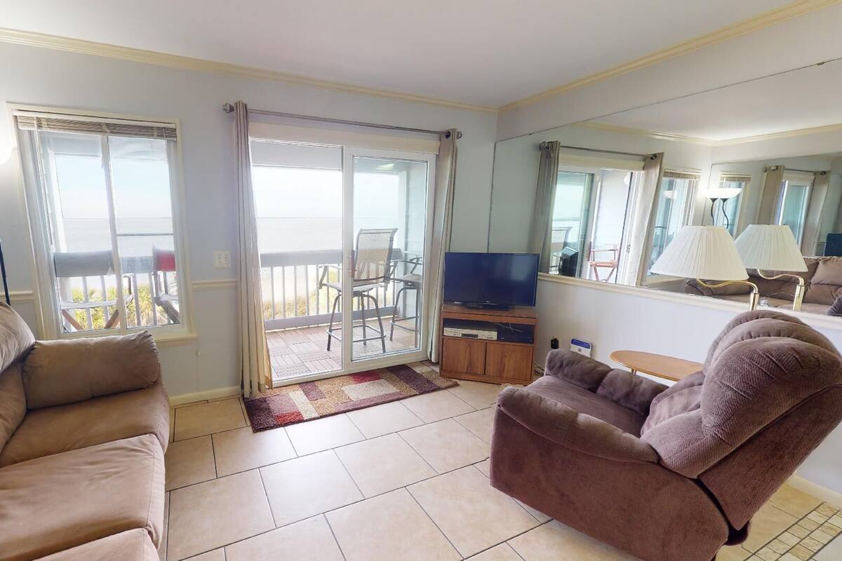 A living room with a sofa, armchair, TV, and a balcony with a view.