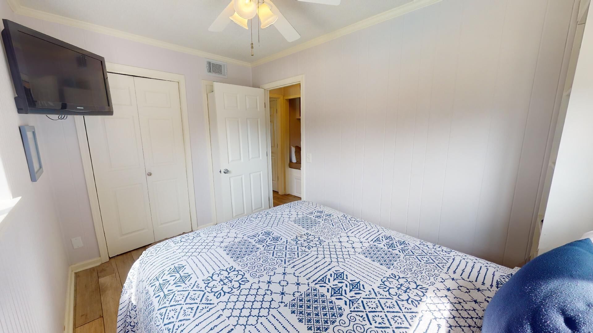 A bedroom with a bed, a TV mounted on the wall, and a ceiling fan.