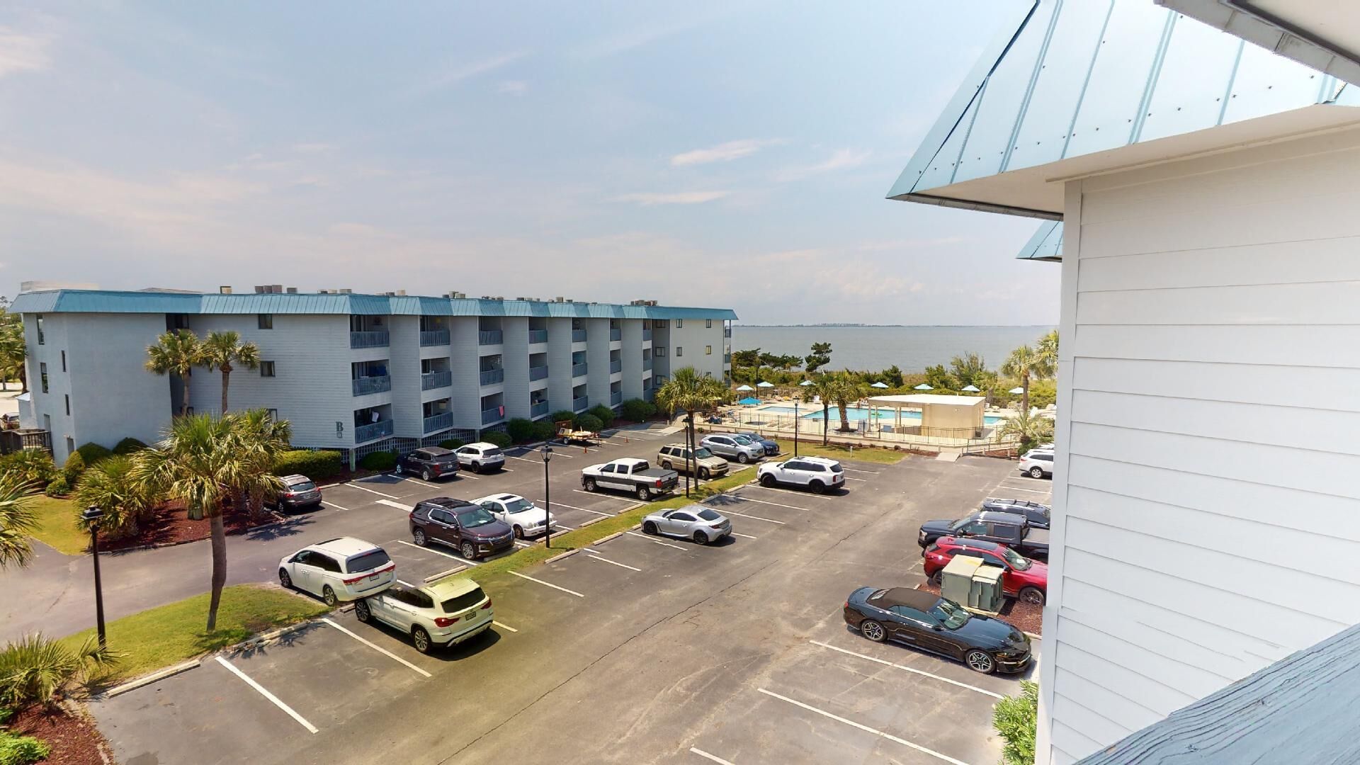 A hotel with a parking lot, a pool area, and a view of the ocean.