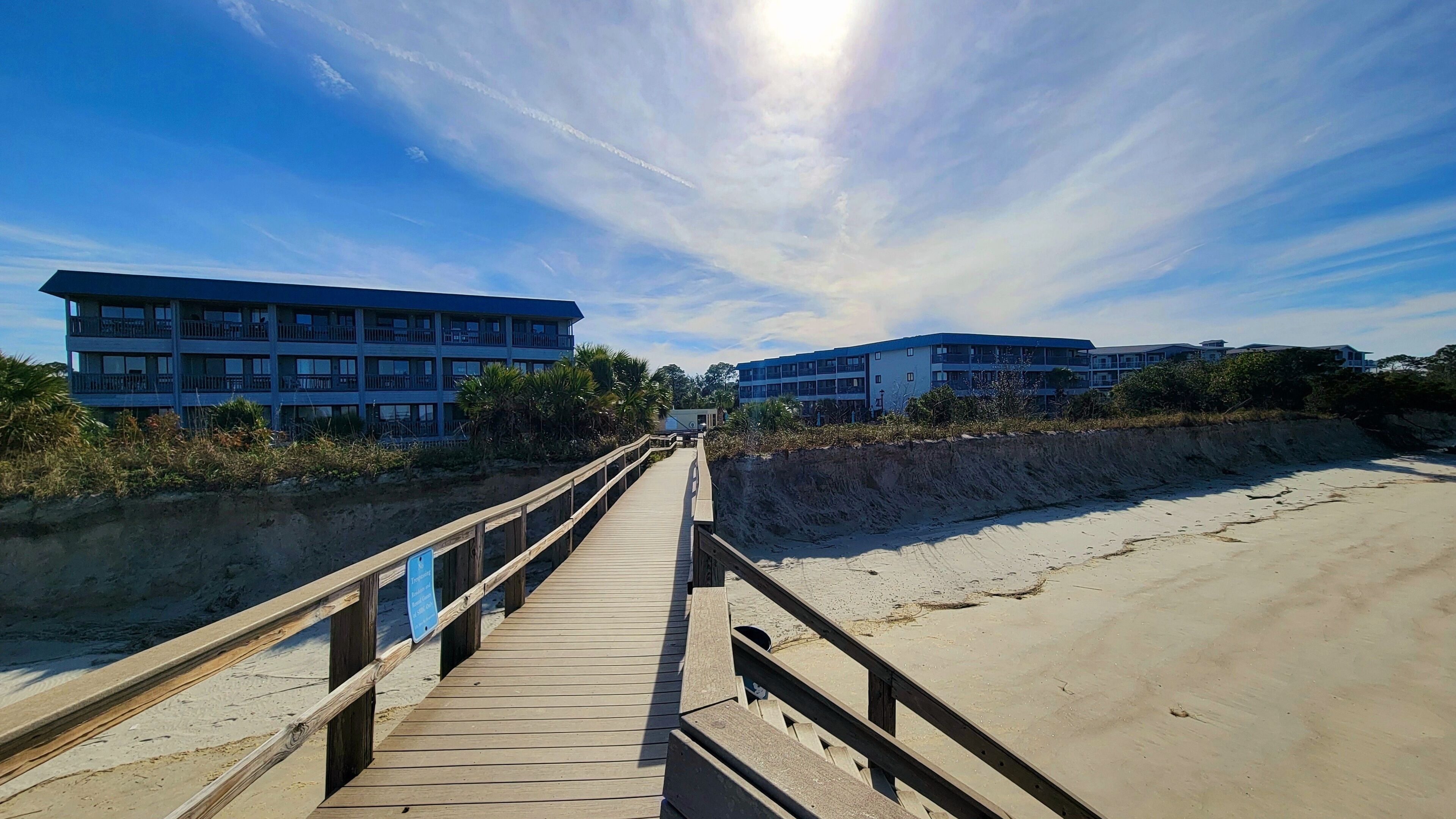 A wooden boardwalk leading to beachfront buildings with multiple balconies.