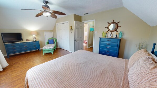A bedroom with a bed, a dresser, a television, and a ceiling fan.