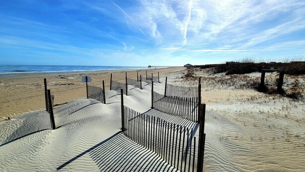 A sandy beach with a wooden fence leading to the water. - Sea Tybee by Tybee Vacation Rentals (Tybee Island)