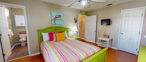 A bedroom with a green bed, a ceiling fan, a television, and a bathroom with a toilet and cabinet.