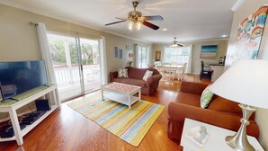 A spacious living room with a television, sofa, coffee table, and a ceiling fan. - Sea Tybee by Tybee Vacation Rentals (Tybee Island)