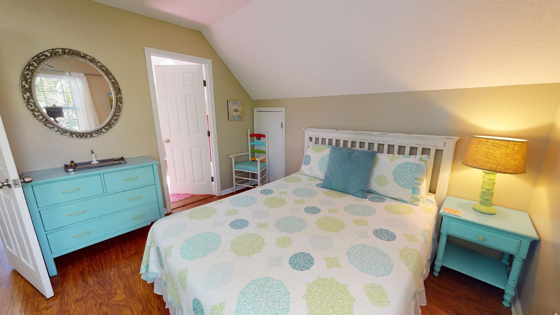 A bedroom with a bed, dresser, nightstand, lamp, and a mirror.