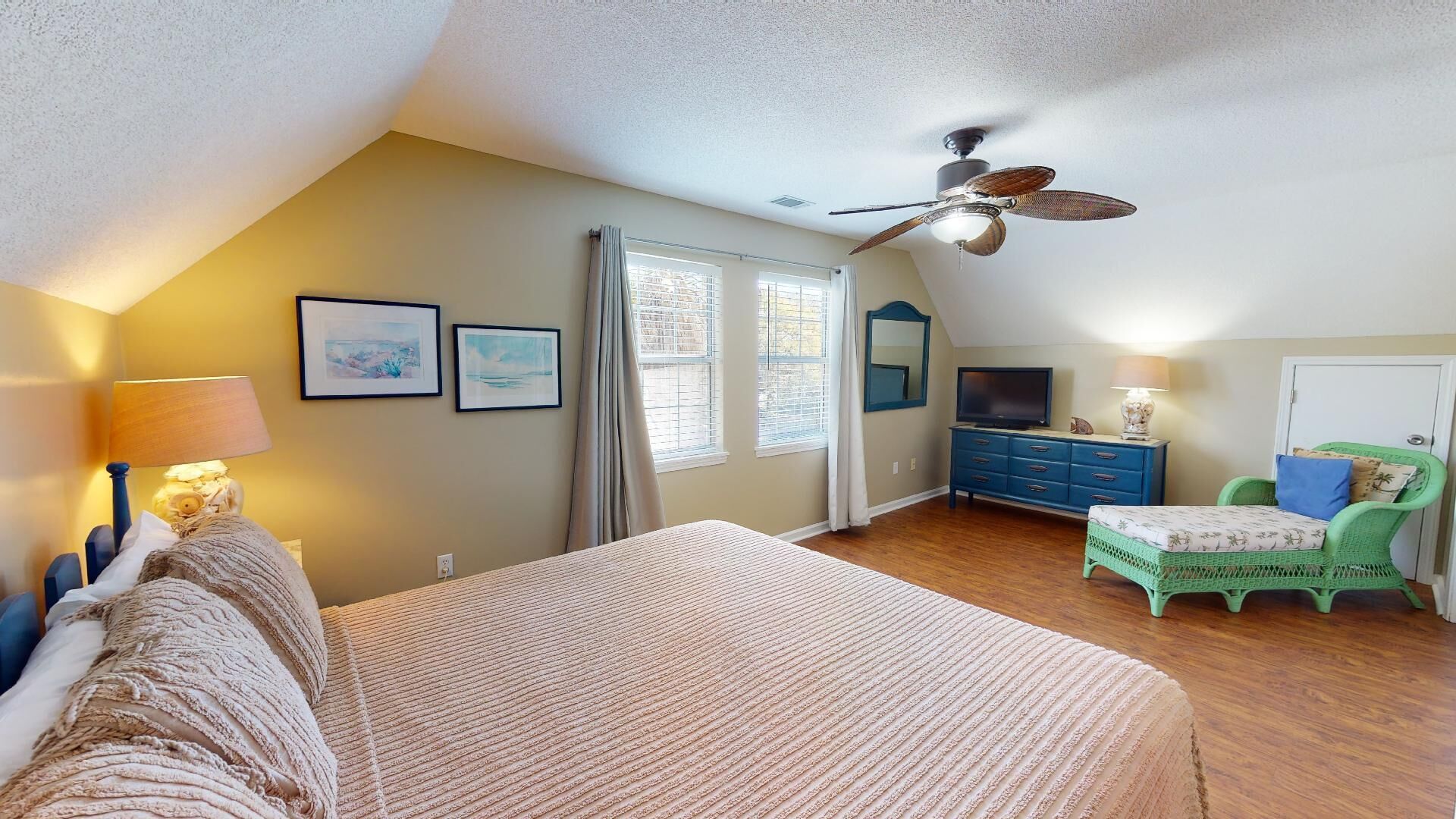 A bedroom with a bed, a dresser, a television, and a ceiling fan.