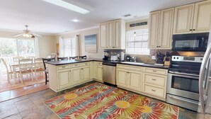 A kitchen with cream-colored cabinets, a black countertop, a stainless steel dishwasher, a microwave, and an oven. There's a colorful rug on the floor and a ceiling fan. - Sea Tybee by Tybee Vacation Rentals (Tybee Island)