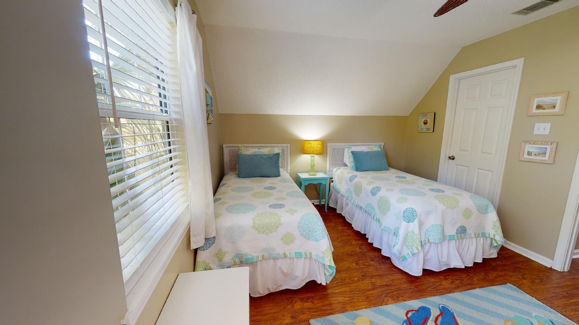 A bedroom with two beds, a nightstand, a lamp, and a window with blinds.