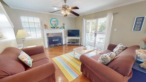 A living room with two brown sofas, a coffee table, a fireplace, a television, and a large window with curtains. - Sea Tybee by Tybee Vacation Rentals (Tybee Island)