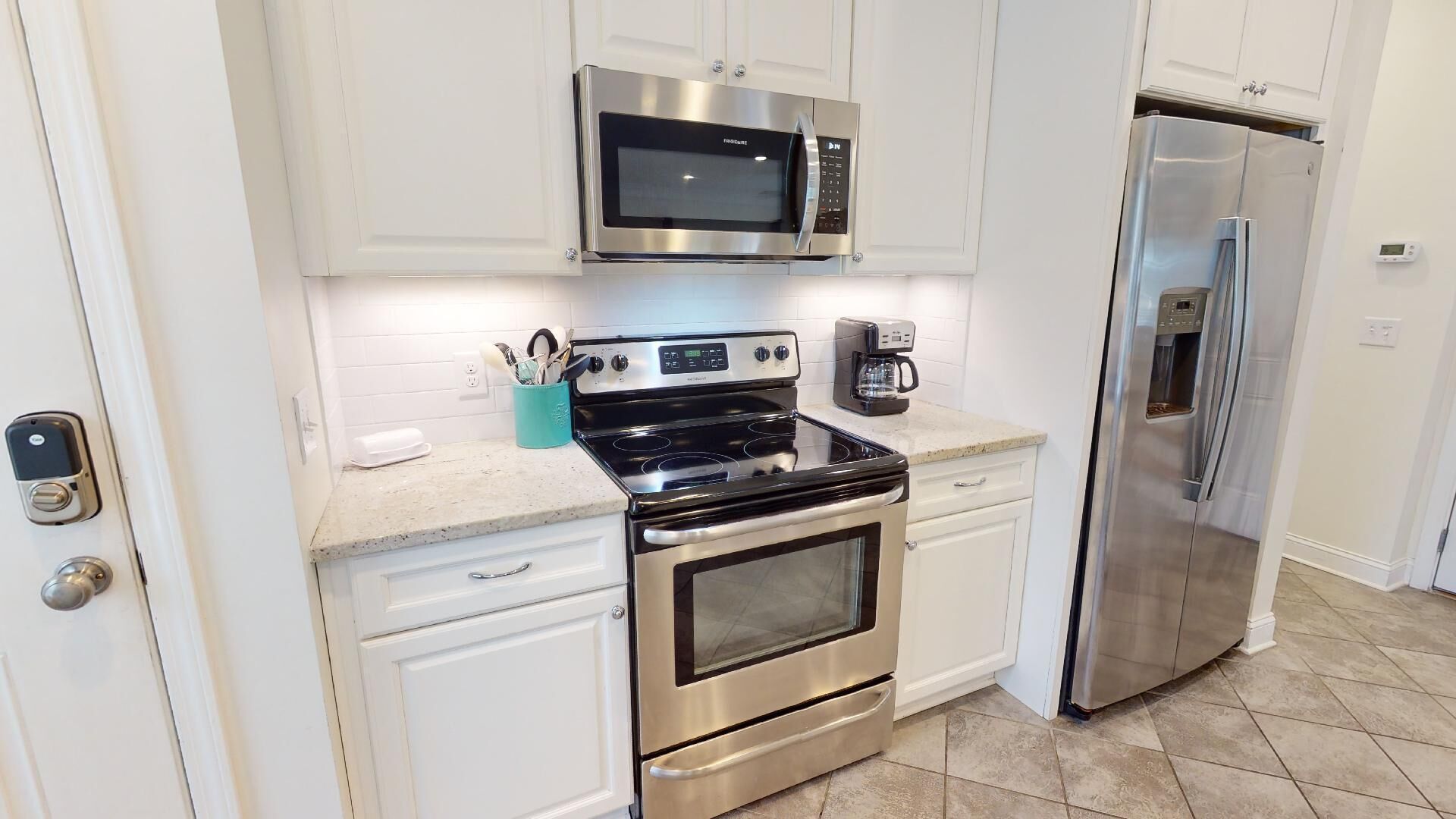 A modern kitchen with stainless steel appliances, white cabinetry, and a tiled floor.