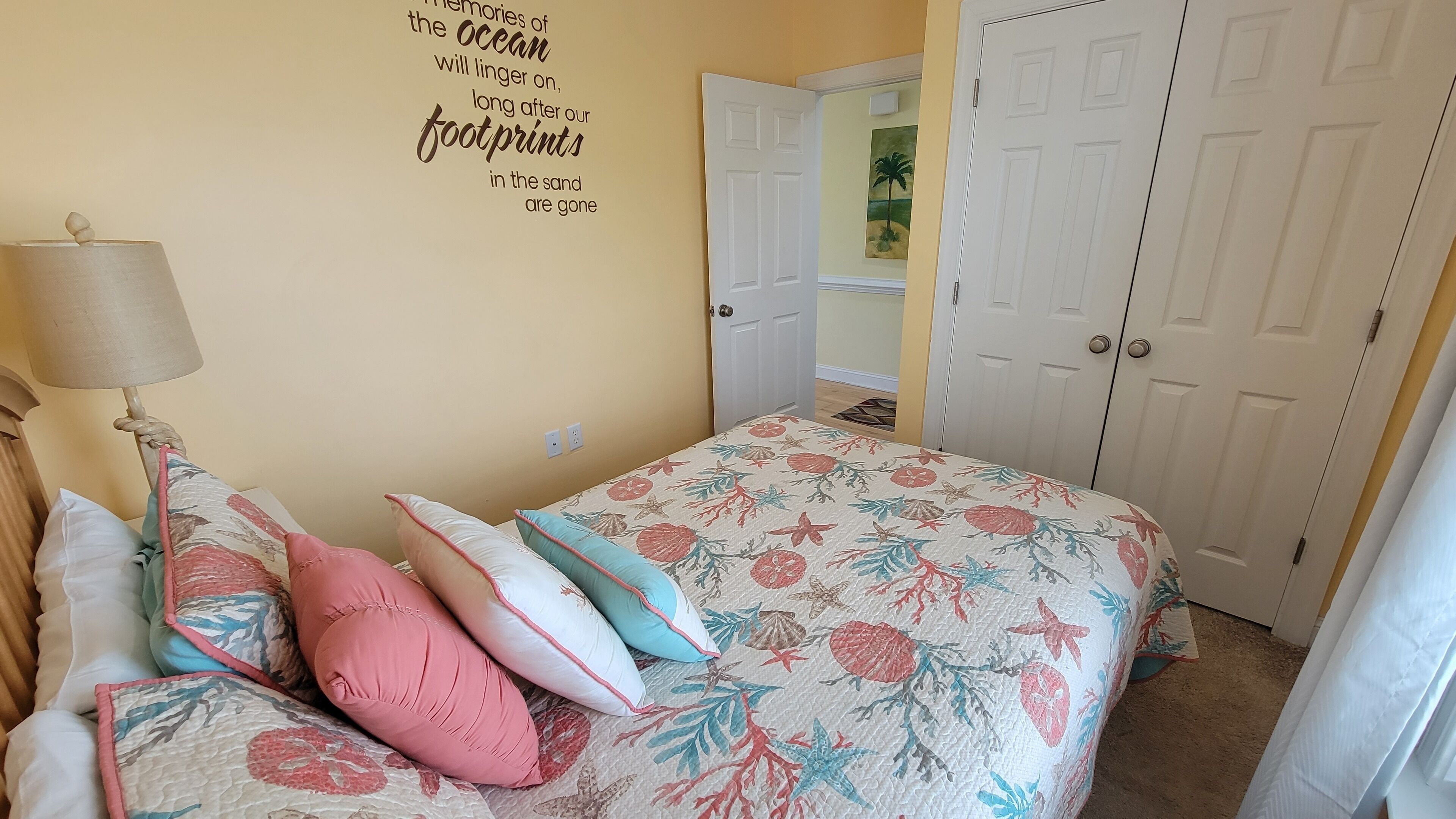 Un dormitorio con cama, almohadas, una lámpara, una puerta y una pared con una cita.