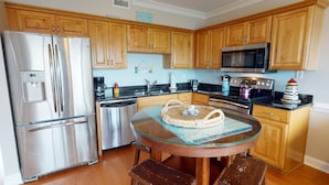 A modern kitchen with stainless steel appliances, wooden cabinets, and a glass-top dining table. - Silver Shores by Tybee Vacation Rentals (Tybee Island)