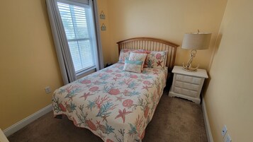 Un dormitorio con cama, mesita de noche, lámpara y ventana con persianas.