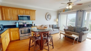 A modern kitchen with wooden cabinets, stainless steel appliances, and a round glass table with stools. - Silver Shores by Tybee Vacation Rentals (Tybee Island)