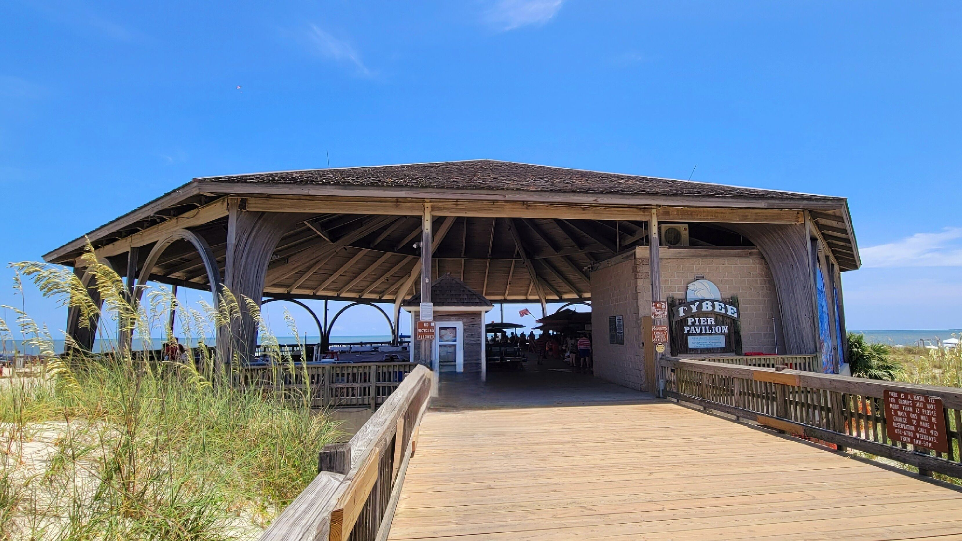 A pier pavilion with a wooden roof and a wooden walkway leading to it.