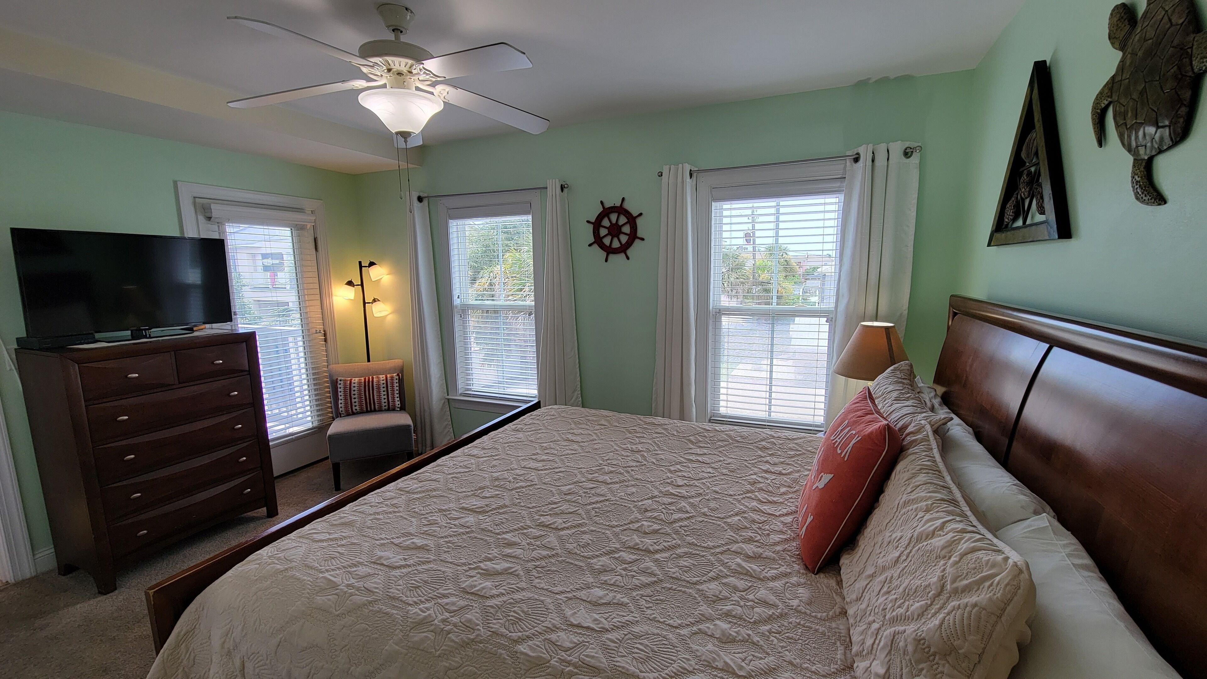 A bedroom with a bed, a dresser, a TV, a ceiling fan, and a window with curtains.
