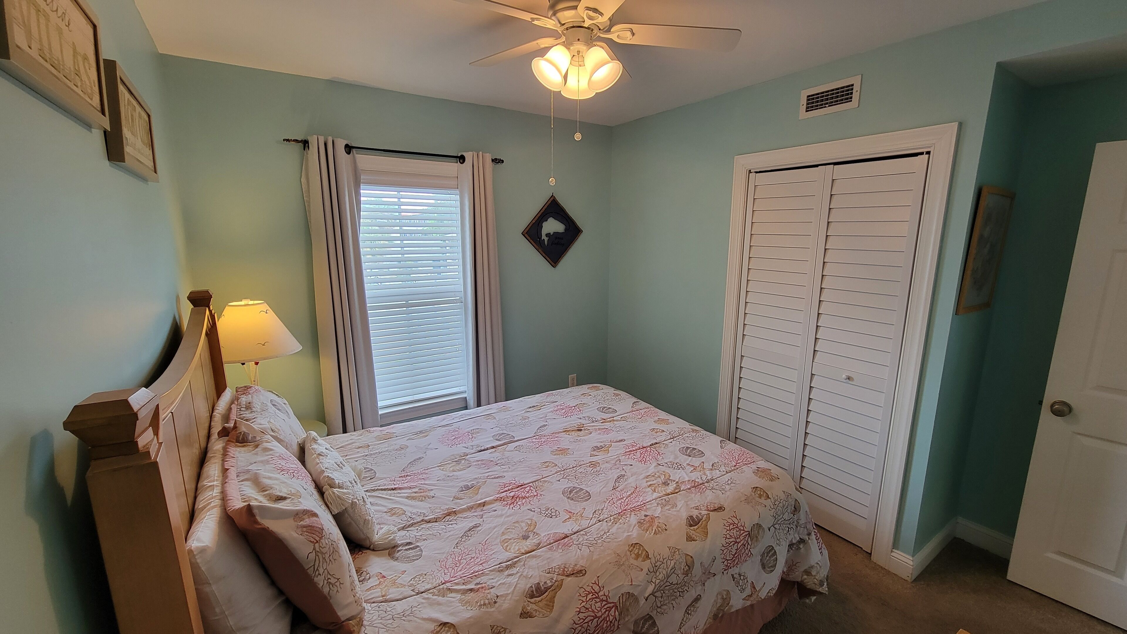 Une chambre à coucher comprenant un lit, une table de chevet, un ventilateur de plafond, une fenêtre avec des rideaux et un placard.