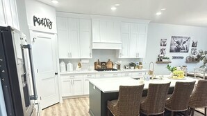 A modern kitchen with white cabinets, a central island with bar stools, and a refrigerator.