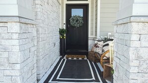 A covered porch with a black door, white brick walls, and a black and white rug.
