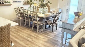 A dining area with a wooden table and chairs, a hanging light fixture, and wall-mounted artwork.