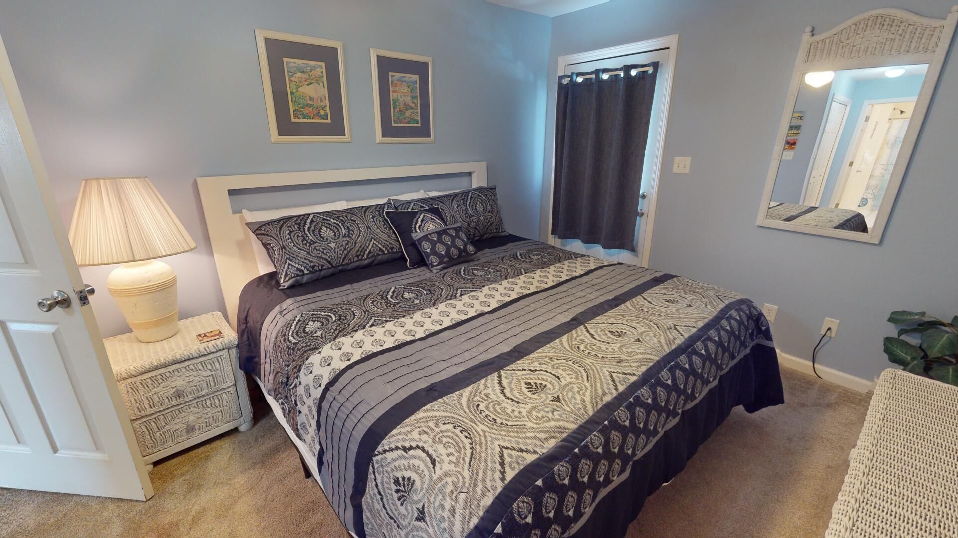 Un dormitorio con cama, mesitas de noche, lámpara, espejo y puerta.