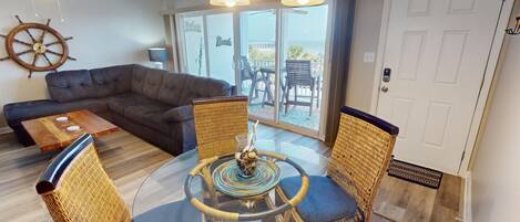 A living room with a dark brown sofa, a glass coffee table, wicker chairs, and a ship's wheel decoration.