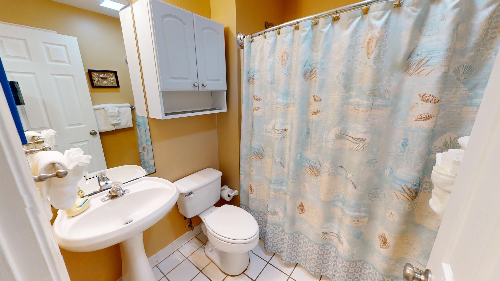 A bathroom with a white sink, toilet, and a shower curtain with a nautical theme.