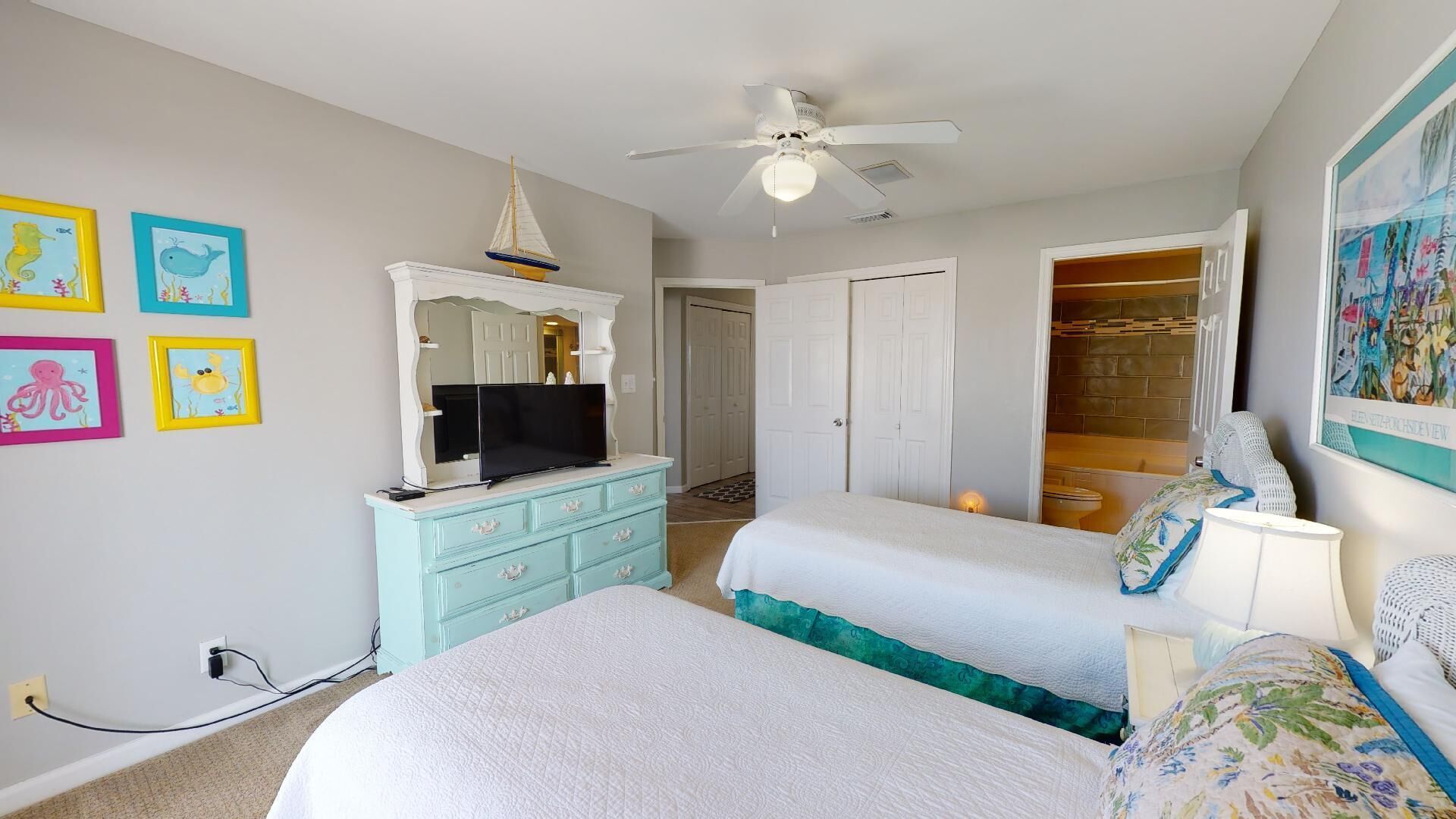 Une chambre avec deux lits, un téléviseur posé sur une commode, un ventilateur de plafond et un placard avec vue.
