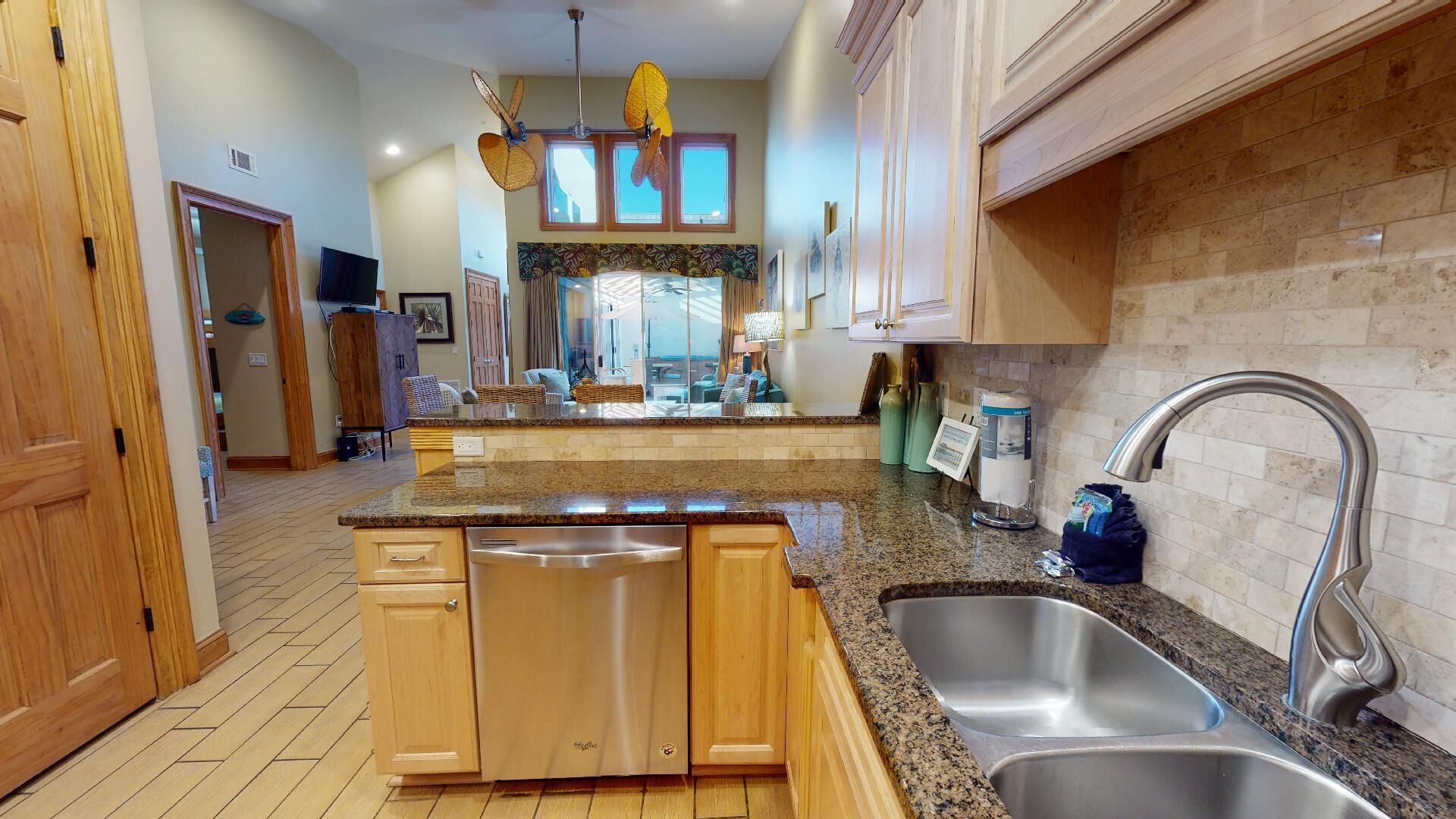 Una cocina con encimeras de granito, electrodomésticos de acero inoxidable, armarios de madera y un amplio ventanal con vistas a la sala de estar.