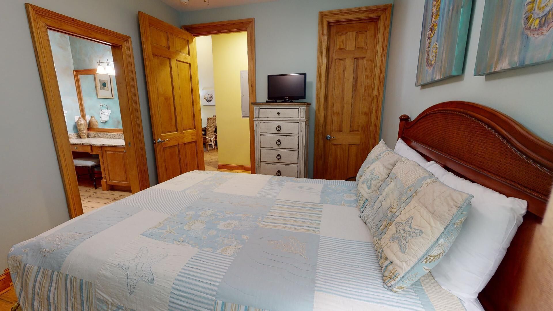Un dormitorio con cama, cómoda, televisión y obras de arte en las paredes.