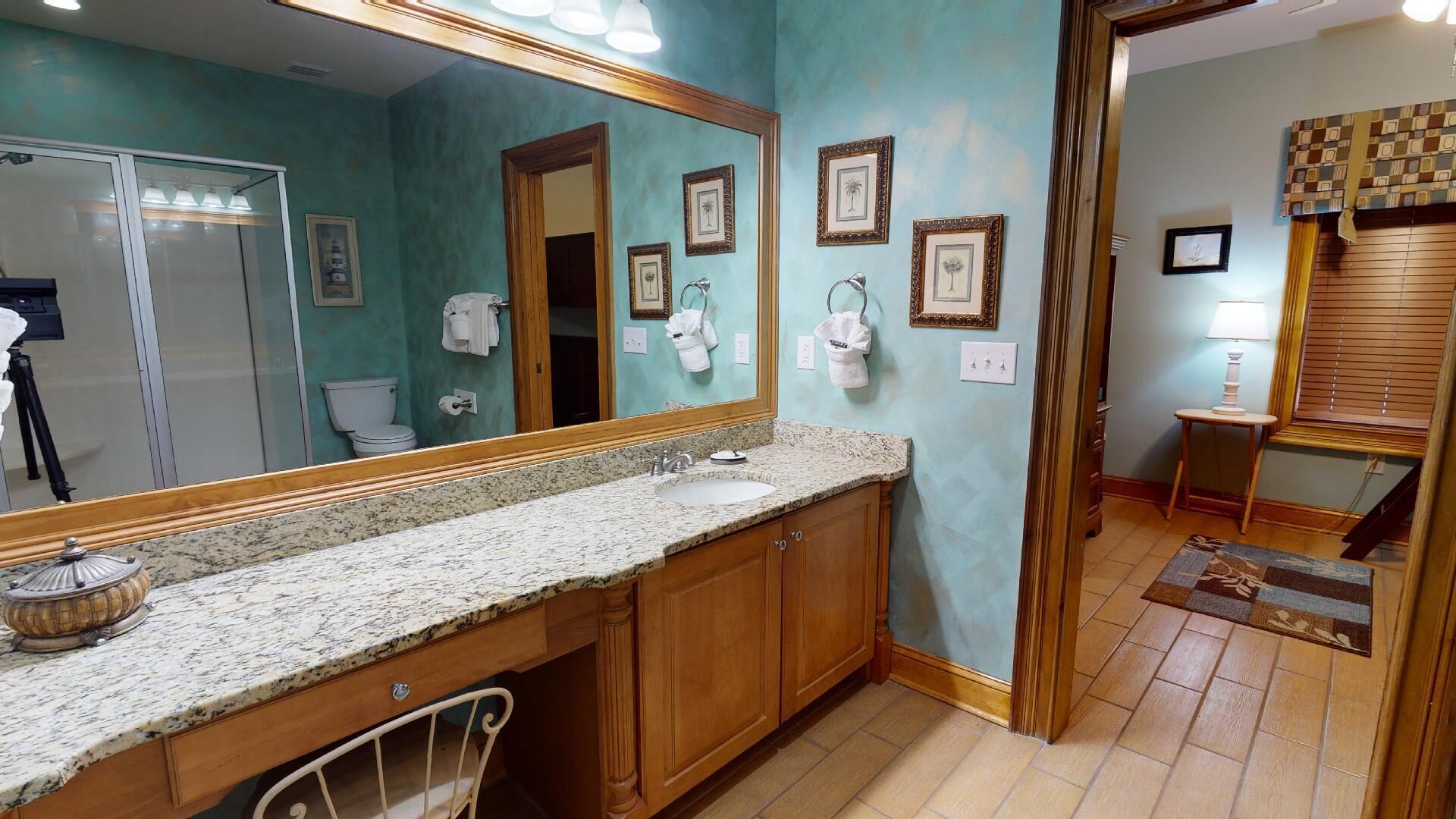 Une salle de bain dotée d’un comptoir en granit, de meubles en bois, d’un grand miroir et de tableaux encadrés accrochés au mur.