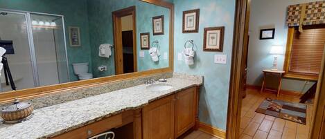 A bathroom with a granite countertop, wooden cabinets, a large mirror, and framed pictures on the wall.