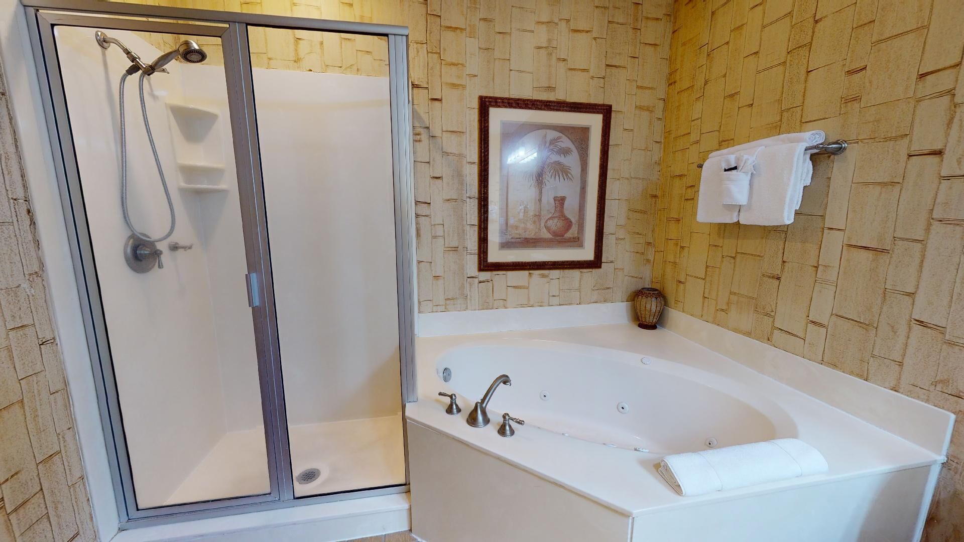 A bathroom with a glass-enclosed shower, a freestanding bathtub, and a framed picture on the wall.
