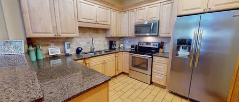 A kitchen with granite countertops, wooden cabinets, a stainless steel refrigerator, a microwave, and an oven.