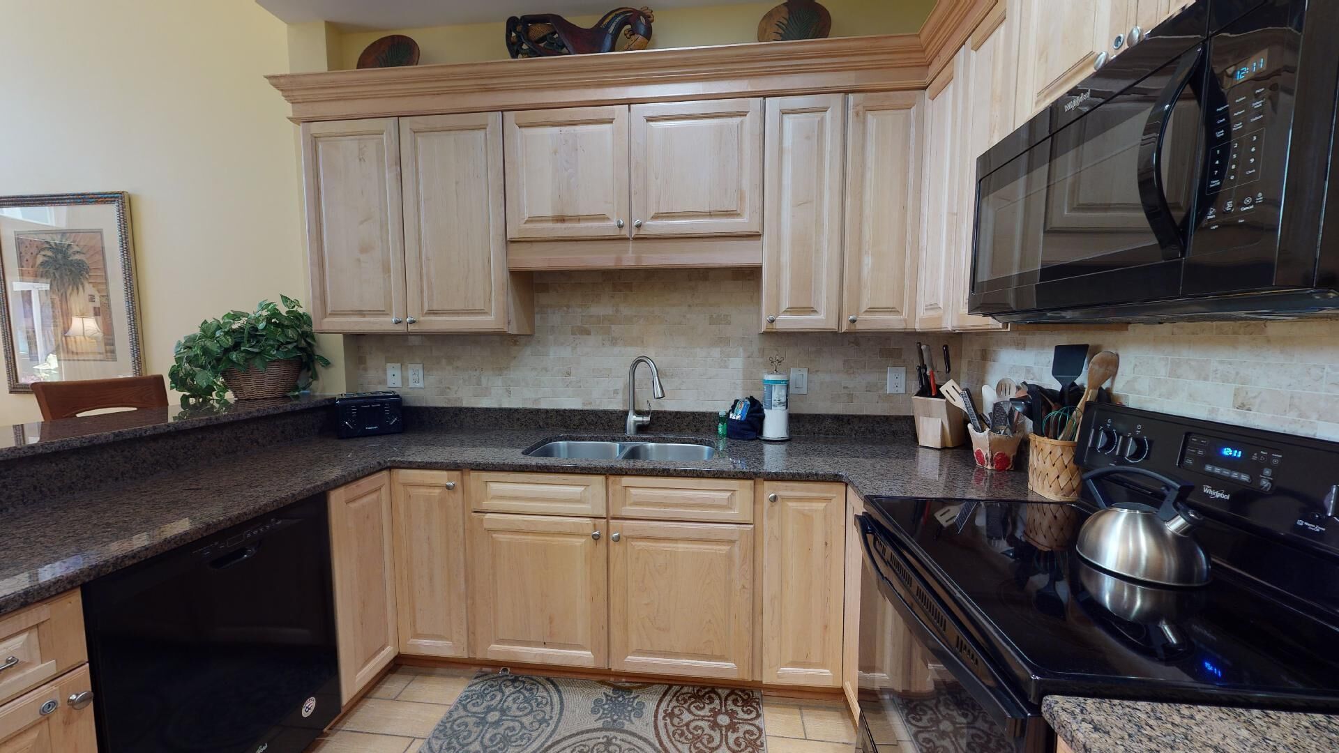 Una cocina con armarios de madera, microondas negro, estufa de acero inoxidable y encimera de granito.