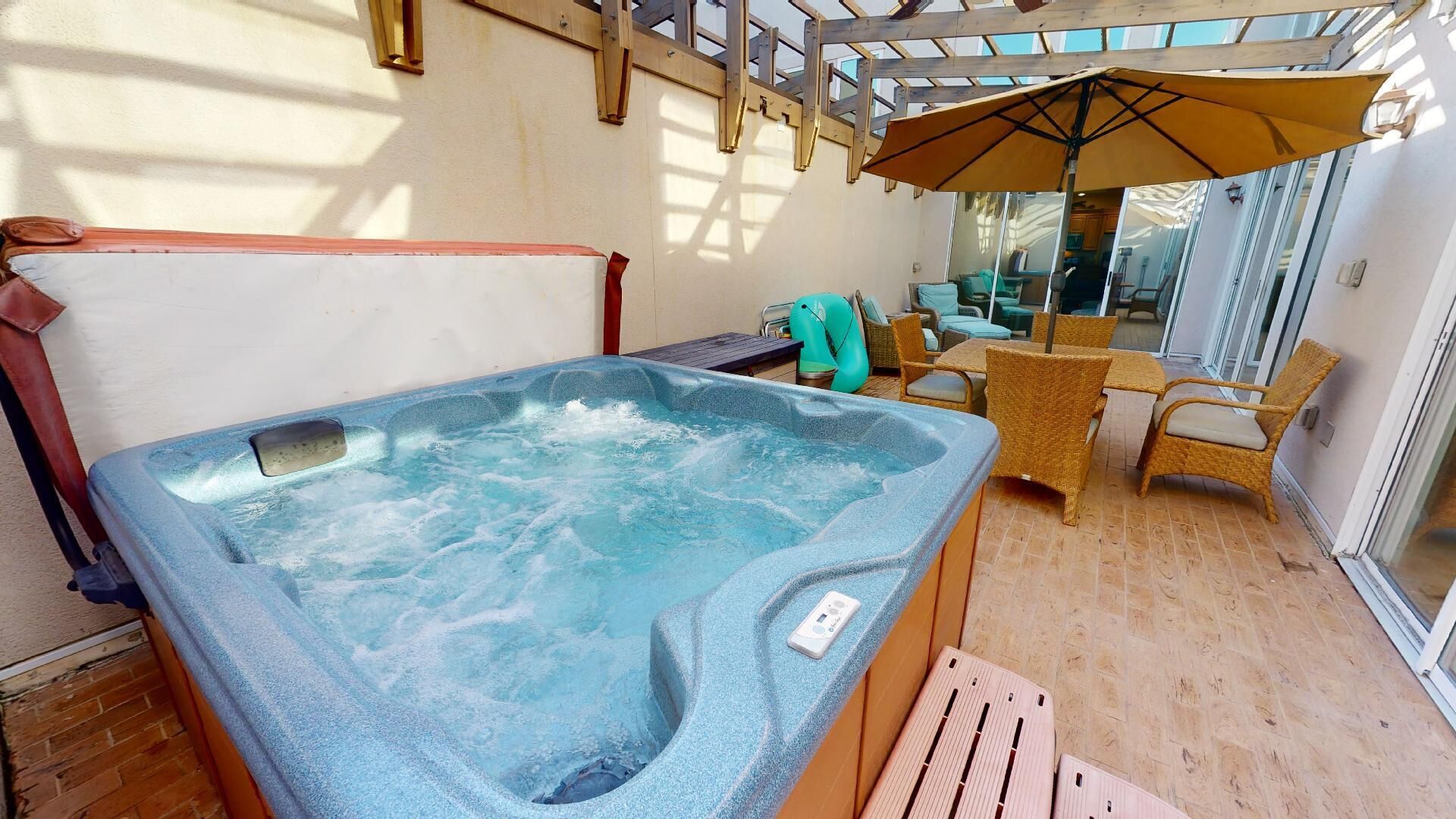 A hot tub in a covered outdoor area with wicker furniture and a patio umbrella.